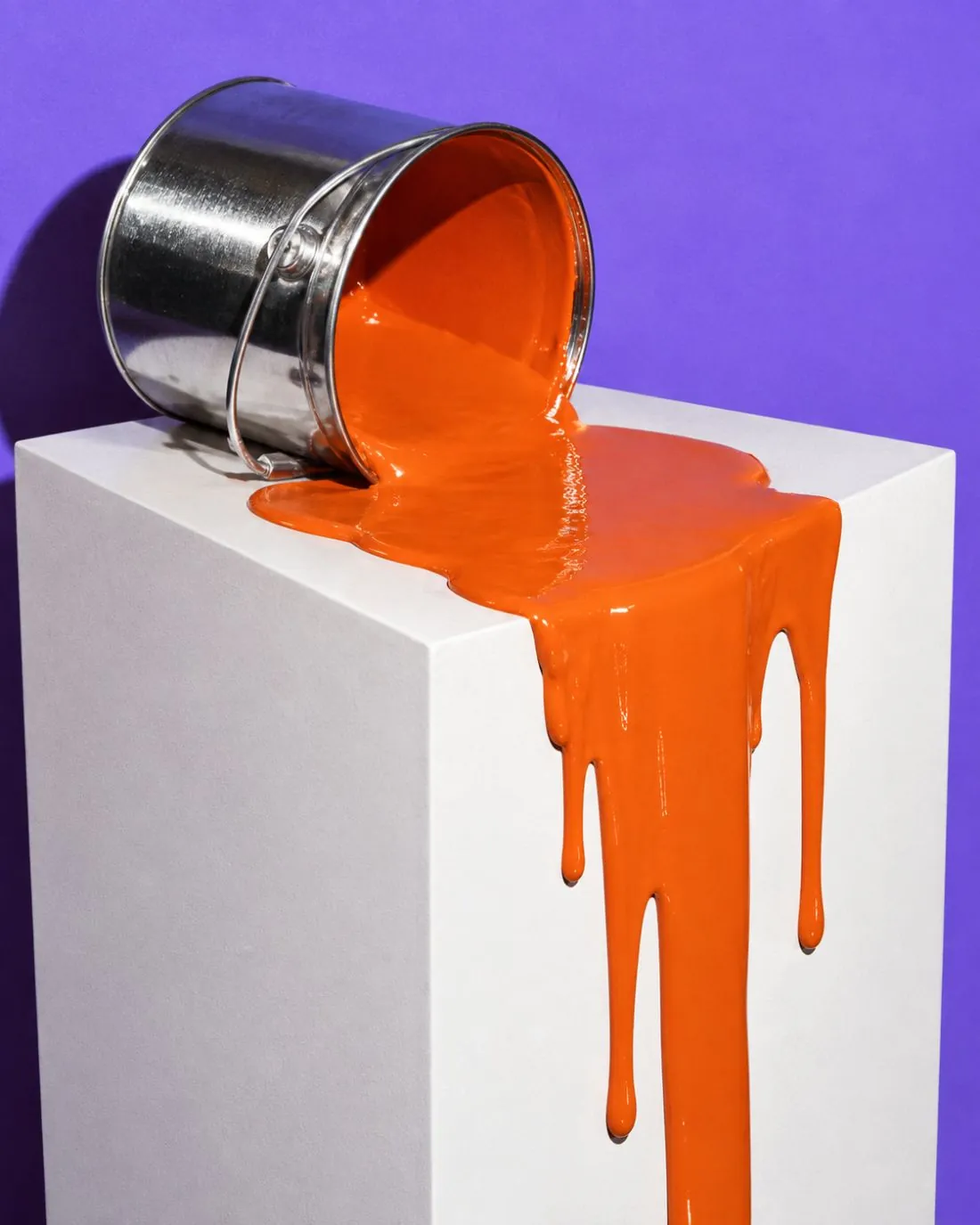 Umgekippter Farbeimer, aus dem orange Farbe an einem weißen Sockel herunterläuft