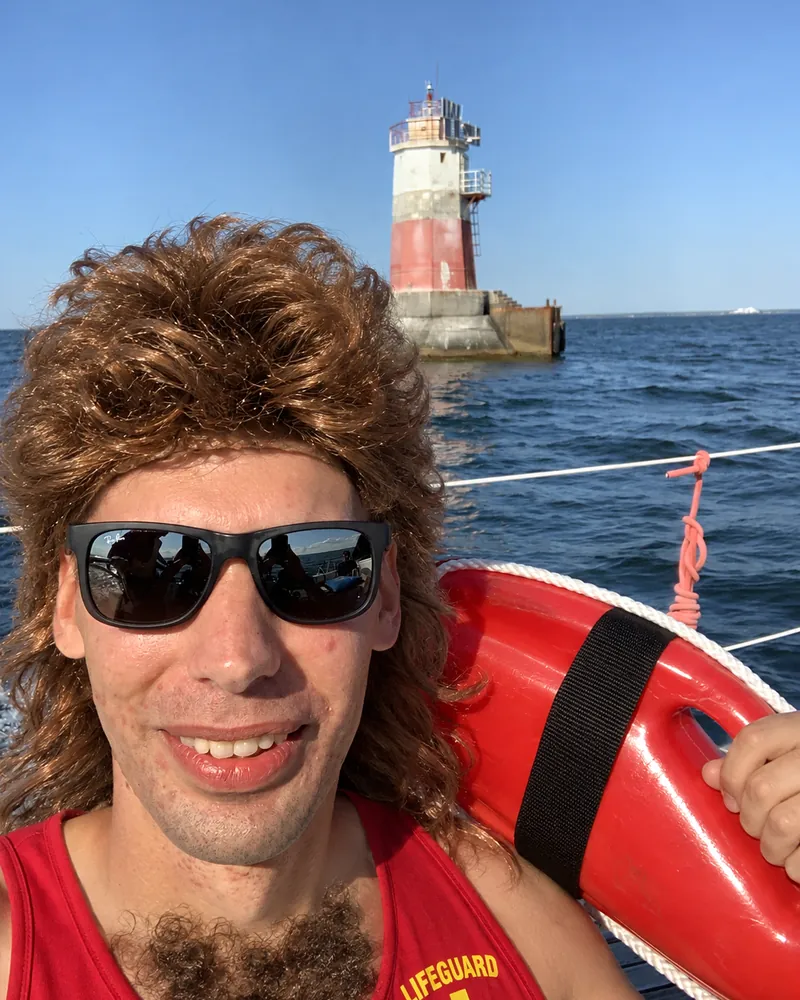 Klemens Arro mullet-parukas, kunstrinnakarvade ja vetelpäästja pluusiga, käes päästepoi